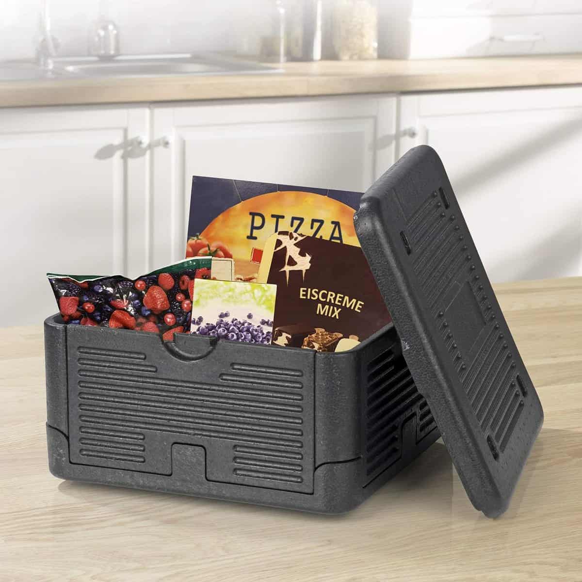 Eine schwarze isolierte Lebensmittelbox mit abgenommenem Deckel zeigt Tiefkühlpizza, gemischte Beeren und andere verpackte Tiefkühlkost auf einer Küchenzeile.
